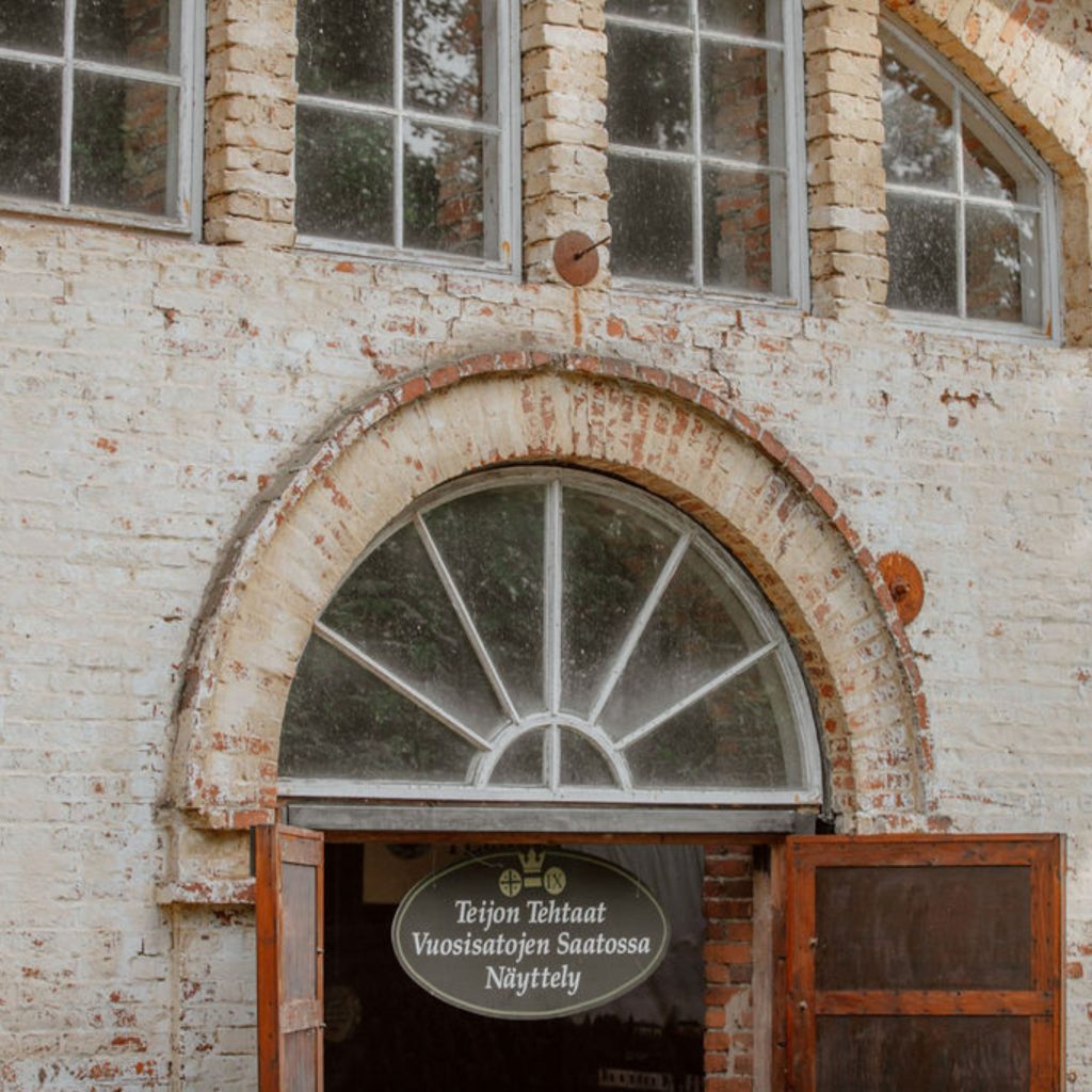 Kuvassa oven yläosa, jossa Mathildedalin Historianäyttelyn kyltti ja oven yläpuolella kaunis kaari-ikkuna.