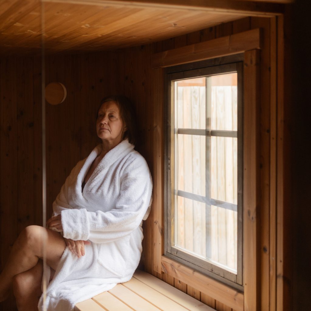 Nainen istuu rentoutuneena kylpytakki päällä puisessa saunassa.