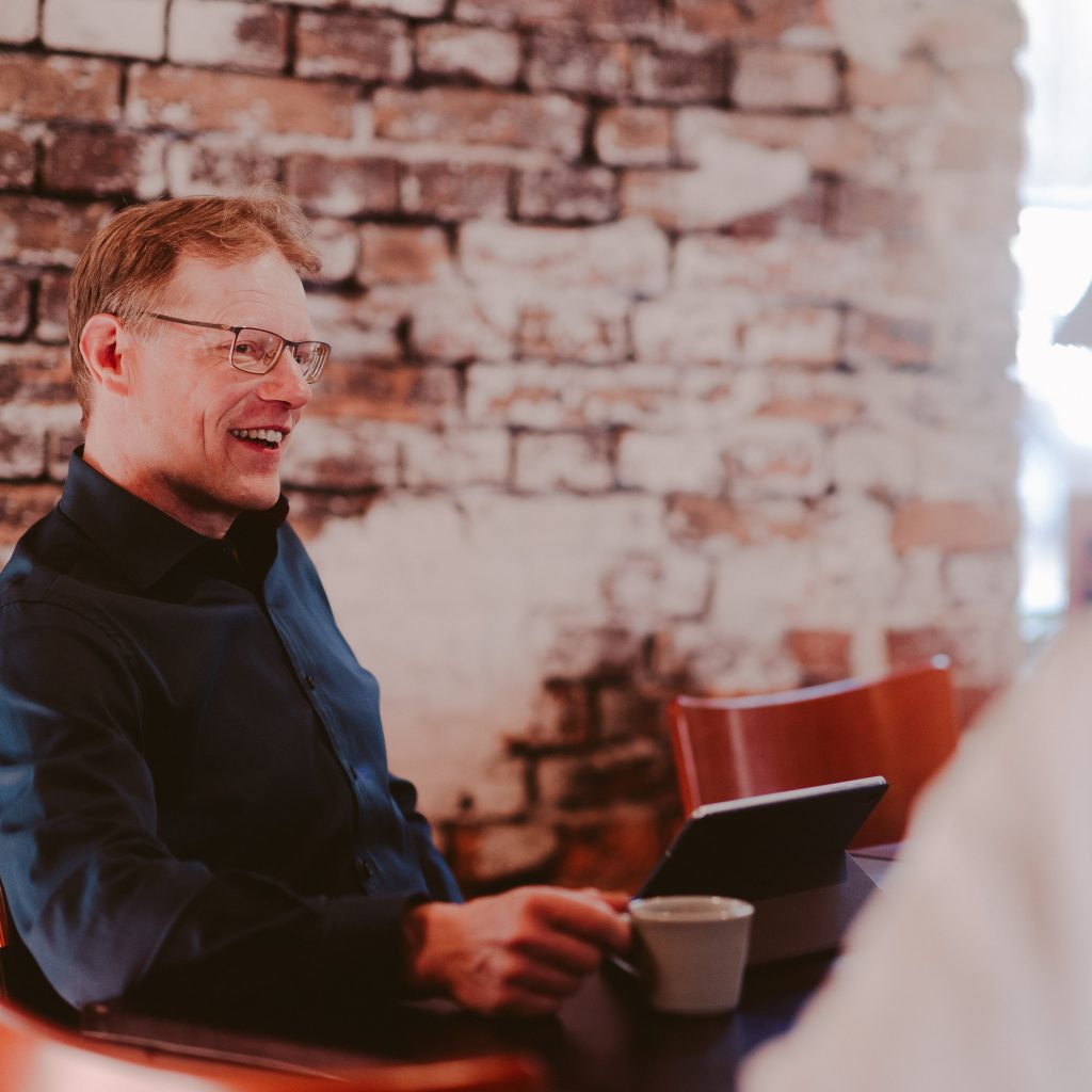 Mies istuu kahvikuppu kädessä kokoustila Kankirautavarastossa punatiilisen seinän edessä.