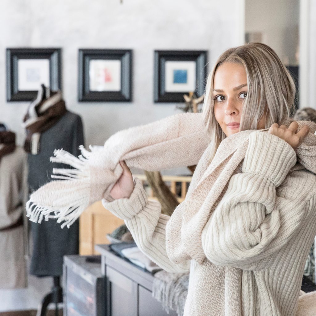 Vaaleahiuksinen nainen kokeilee alpakan villasta tehtyä huivia Ruukin Kehräämön puodissa.