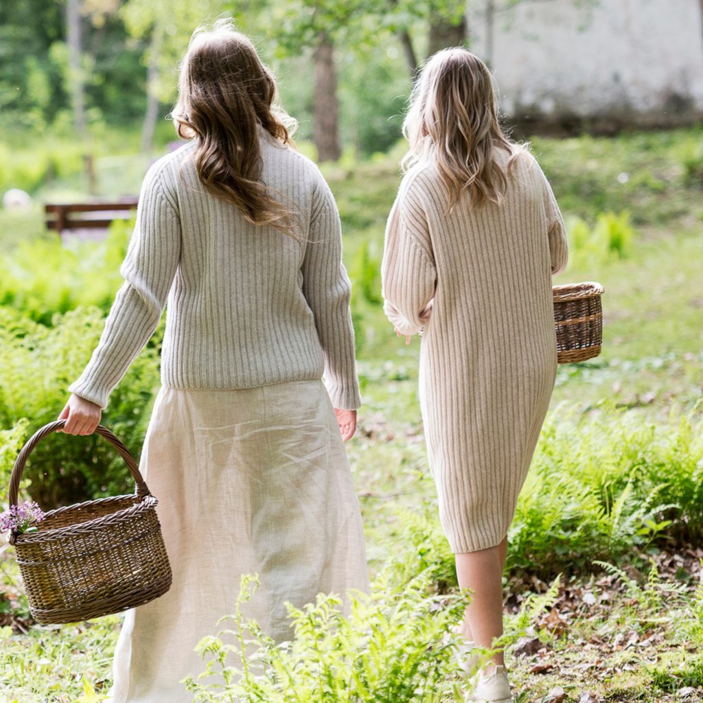 Kaksi naista kävelee korit kädessä nurmikolla selkä kameraan päin.