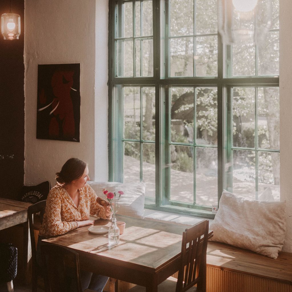 Nainen istuu kahvilla Café Mathildedalissa isojen ikkunoiden edessä ja katsoo ulos ikkunasta.