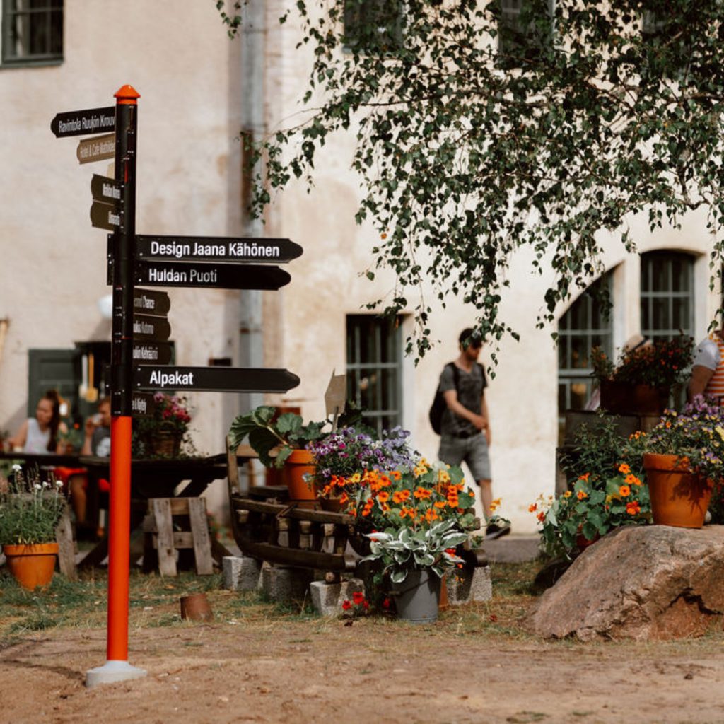 Opastutskyltti Mathildedalin Ruukkitehtailla. Kyltin umpärillä kukkaistutuksia.