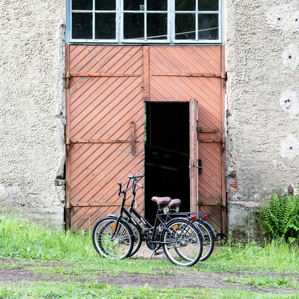 Kaksi jopomallista pyörää ison vanhan puisen oranssin värisen oven edustalla.