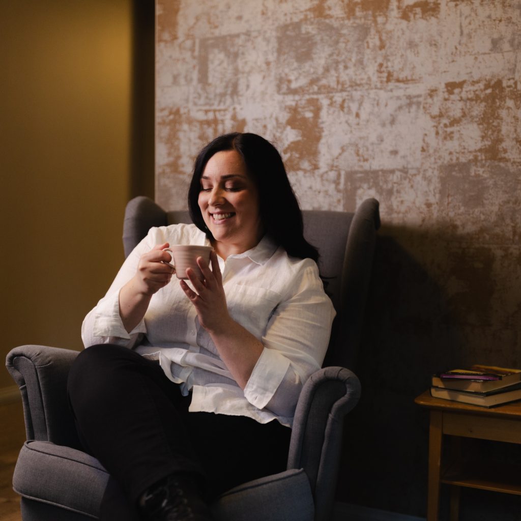 Nainen istuu ja nautiskelee nojatuolissa Hotel Mathildedalin aulassa.